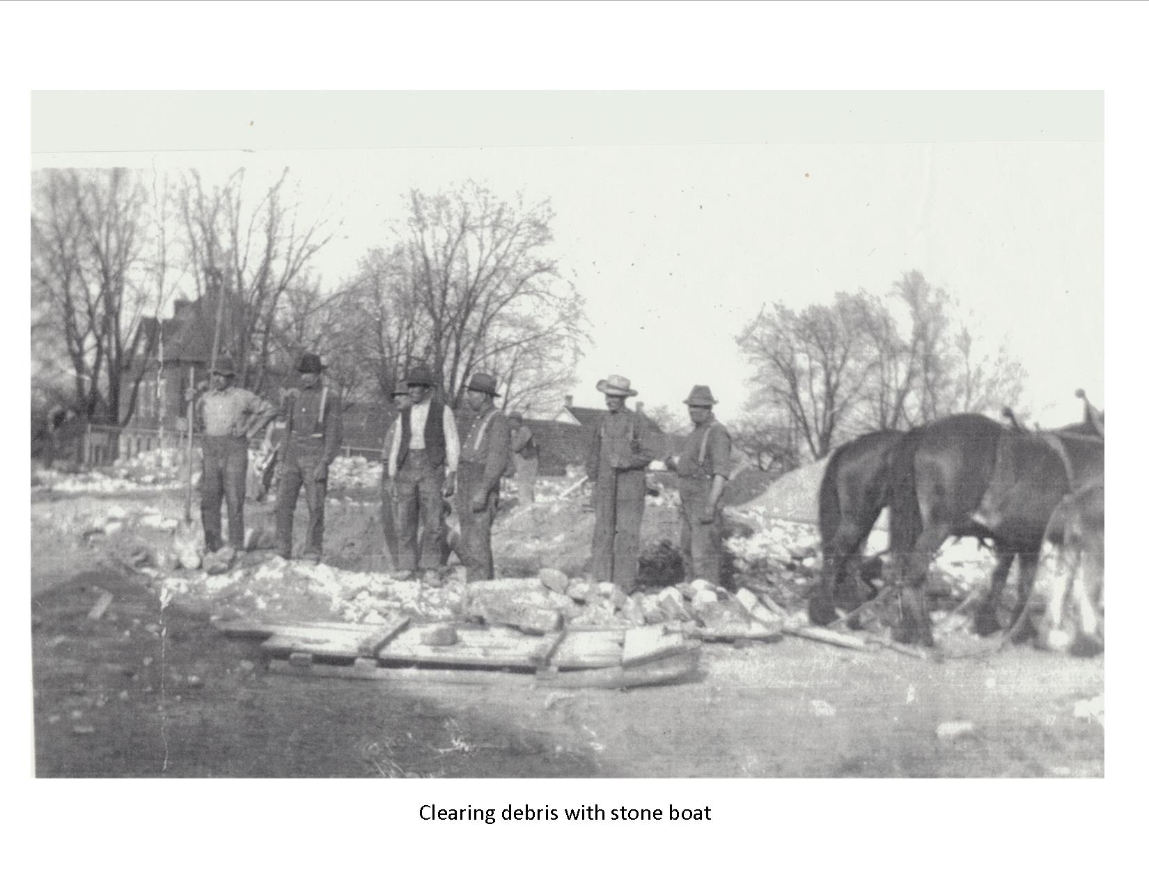 7 men standing in pile of rubble with team of horses hooked to a sliding platform called a 'stone boat'